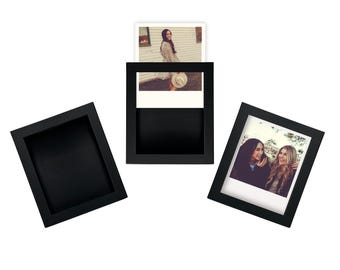 May include: Three black square photo frames, one empty, two with photos. One photo shows a woman in a field, the other shows two women smiling. The frames are arranged on a white background.