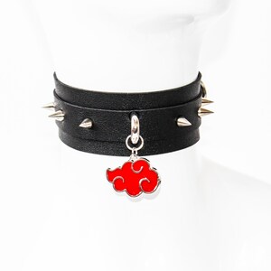 Puede incluir: Collar gargantilla negro con púas plateadas y un colgante de nube roja. El collar de cuero negro tiene púas plateadas alrededor. Un dije de nube roja cuelga en el centro.