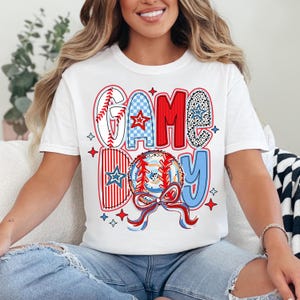 May include: White t-shirt with a red, white, and blue graphic that says "GAME DAY" with a baseball and a bow.