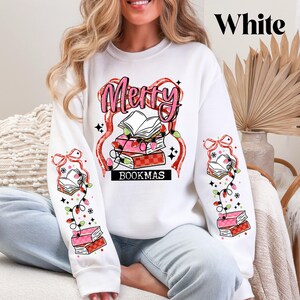 May include: White sweatshirt with a festive "Merry BOOKMAS" design. The graphic features a stack of books, string lights, and the word "Merry" in pink. The sleeves have matching book and light designs.