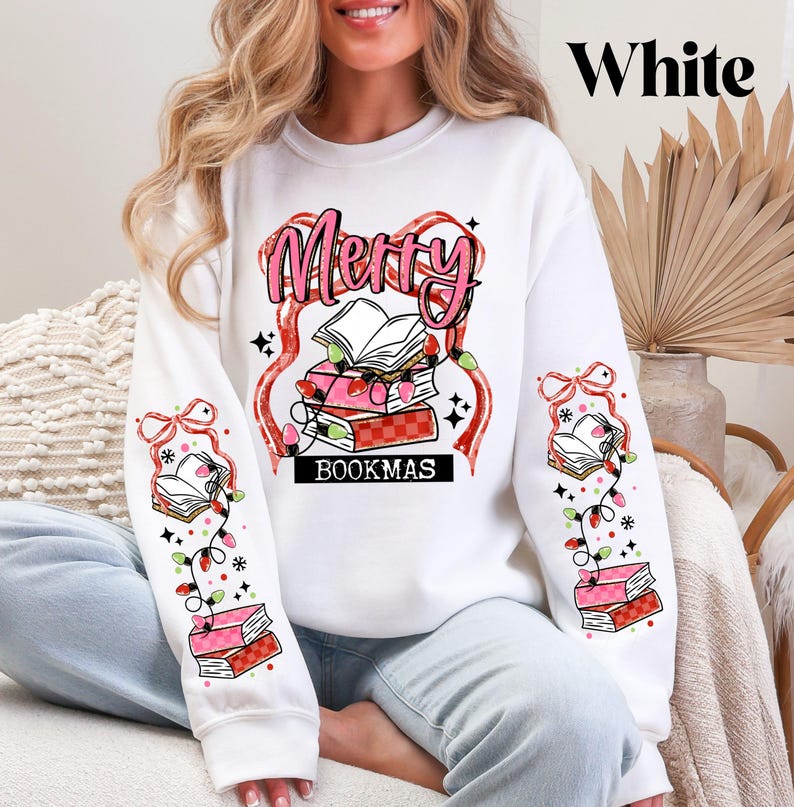 May include: White sweatshirt with a festive "Merry BOOKMAS" design. The graphic features a stack of books, string lights, and the word "Merry" in pink. The sleeves have matching book and light designs.
