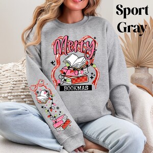 May include: Sport Gray sweatshirt with a festive "Merry Bookmas" design. The design features a stack of books, string lights, and the text "Bookmas". The sleeve has a matching design with books and lights.