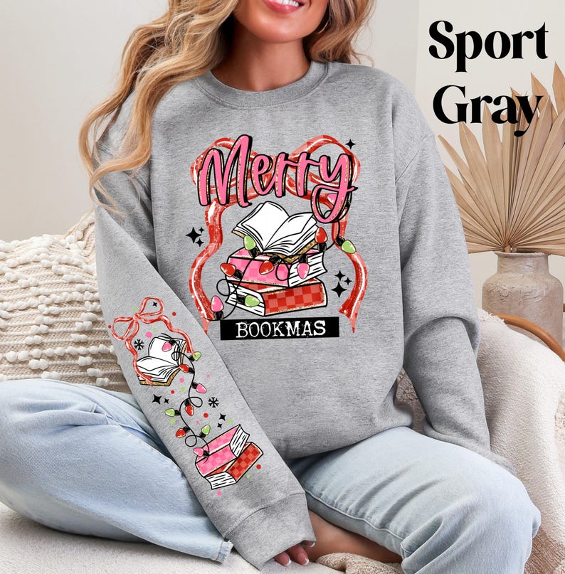 May include: Sport Gray sweatshirt with a festive "Merry Bookmas" design. The design features a stack of books, string lights, and the text "Bookmas". The sleeve has a matching design with books and lights.