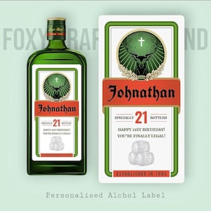 May include: A green glass bottle and a rectangular label featuring a stag head emblem with a cross. The label displays the name Johnathan, the number 21, and the text Happy 21st Birthday! You're Finally Legal! Established in 1999 with barrel graphics.
