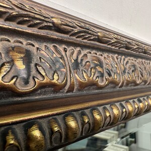 May include: Close-up of a decorative mirror frame with intricate gold and brown detailing. The frame features a raised, ornate design with a textured finish.
