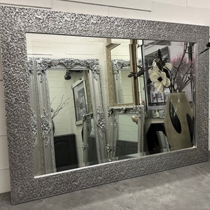 May include: A large silver mirror with a textured frame. The mirror is reflecting other mirrors with ornate frames.
