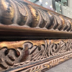 May include: Close-up of a decorative ornate mirror frame with gold and black paint. The frame has a detailed design with intricate carvings and a raised edge.