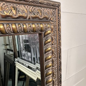May include: A large, ornate mirror with a gold and brown frame. The frame has a detailed, carved design with a rope-like pattern.