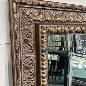 May include: A large, ornate mirror with a gold-toned frame. The frame has a detailed, carved design with a distressed finish.