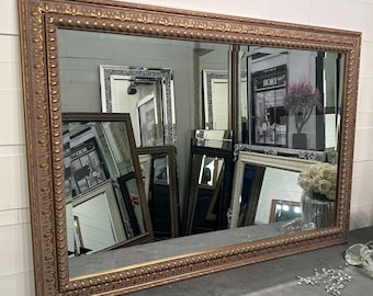 May include: A large, ornate gold-colored mirror with a decorative frame. The frame has a raised, beaded design. The mirror is reflecting other mirrors and a store front with the word "Dior" visible.