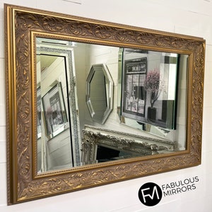 May include: A large, ornate gold mirror with a decorative, carved frame. The mirror is reflecting a room with other mirrors and a sign that says "Dior".