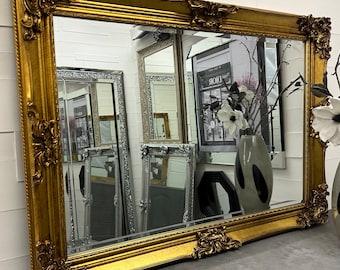 May include: A large, ornate gold-colored mirror with a heavily carved frame. The mirror is reflecting other mirrors and a store display.