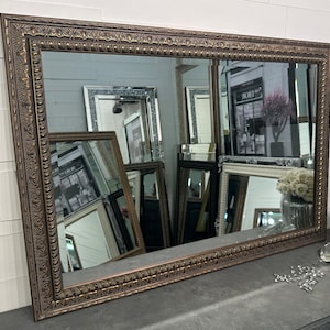May include: A large, rectangular mirror with a wide, ornate, brown frame. The frame has a raised, textured design with a gold finish.