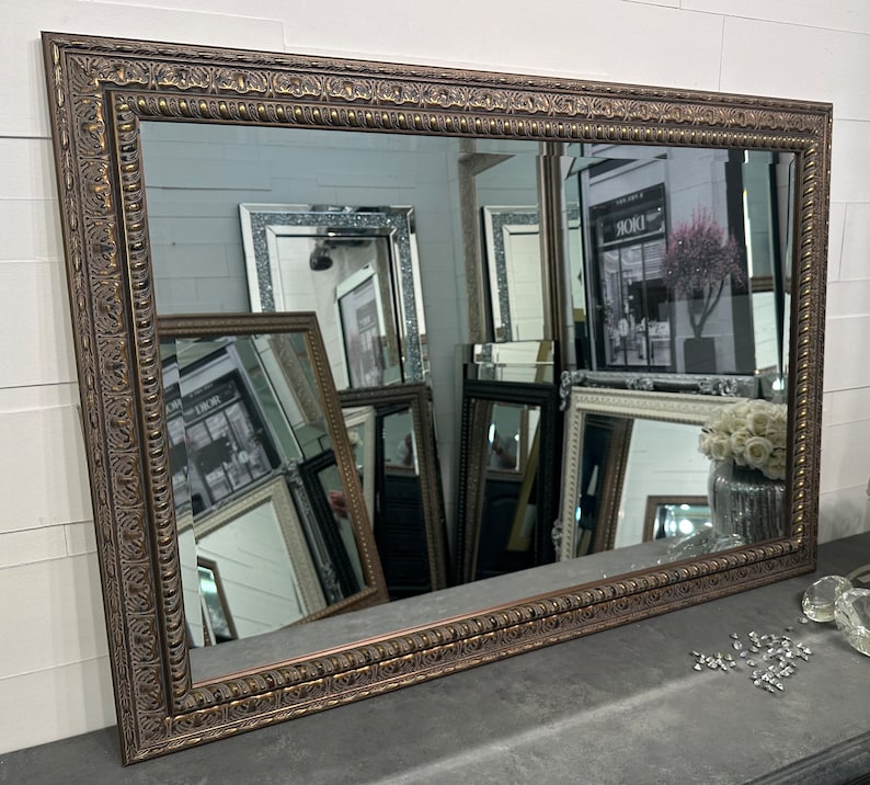 May include: A large, rectangular mirror with a wide, ornate, brown frame. The frame has a raised, textured design with a gold finish.