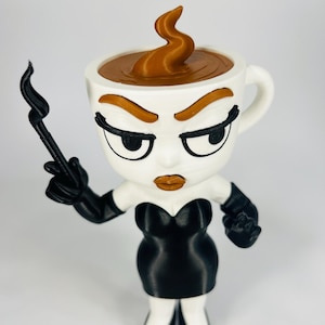 May include: A whimsical figurine of a coffee cup with a face, wearing a black dress and gloves. The coffee cup has a brown liquid and a swirl of coffee steam. The figure has a stern expression with black eyeliner and orange eyebrows.