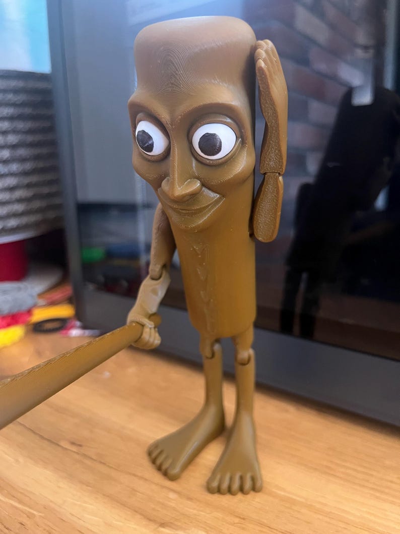 May include: A brown, articulated figurine with large white-eyed features, holding a brown bat. The figure has a rectangular head, a slender body, and bare feet. The figure is posed with one hand on its head.