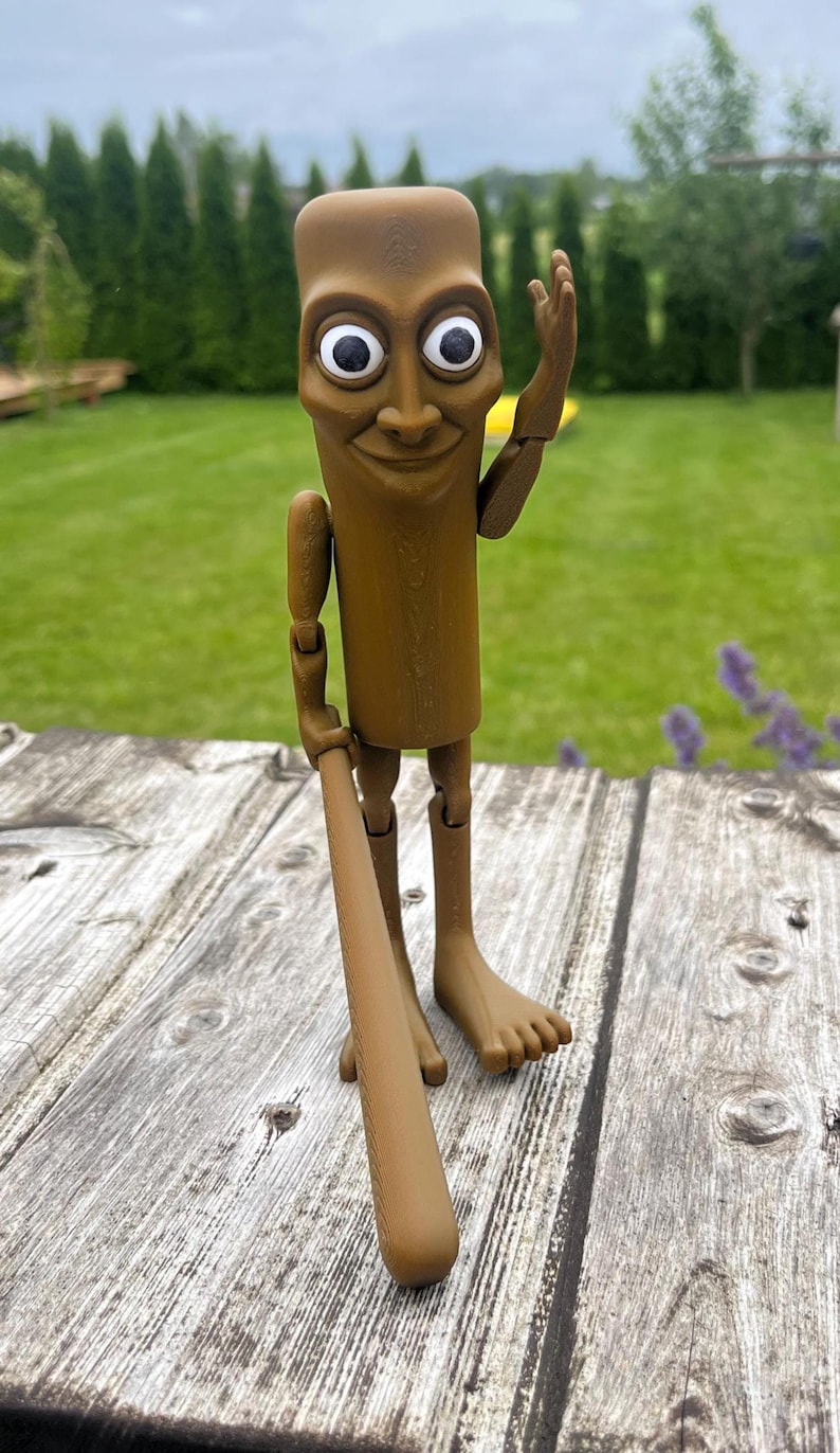 May include: A brown, articulated figurine with a rectangular body, large white-eyed face, and a smiling expression. It holds a brown baseball bat and is posed with one arm raised. The figurine stands on a weathered wooden surface.