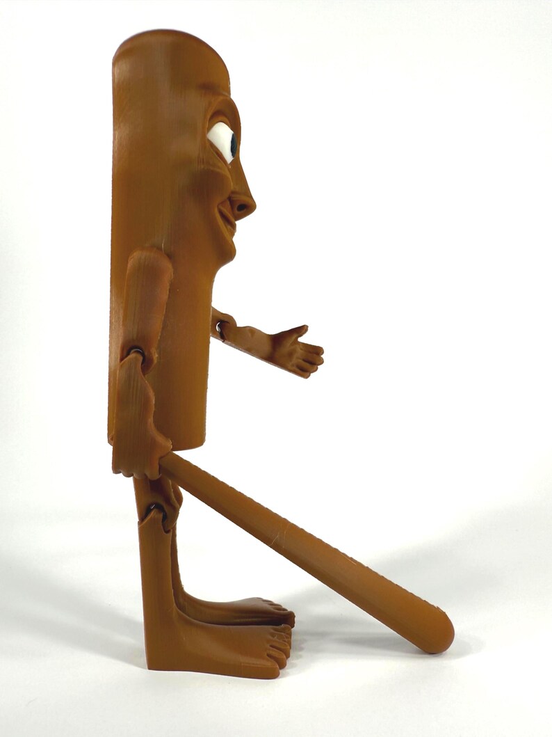 May include: A brown, articulated wooden figure with a smiling face, outstretched arm, and a long, cylindrical body. The figure has a whimsical design, with a long leg extending from the body. The figure is standing on a white surface.