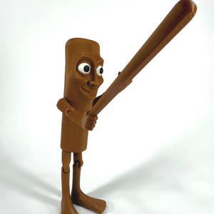 May include: A brown, articulated figurine of a cartoon character holding a baseball bat. The figure has a rectangular body, a smiling face with large eyes, and bare feet. The bat is also brown.