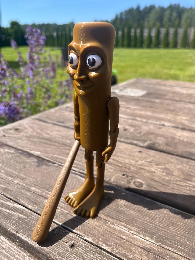 May include: A brown, articulated figurine with a whimsical design. The figure has a cylindrical body, a detailed face with large eyes, and is holding a brown bat. The figurine is standing on a wooden surface.