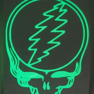 May include: A green and black graphic of a skull with a lightning bolt inside a circle. The skull is smiling and has a single tooth in the front.