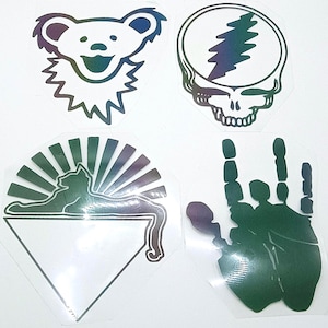 May include: Four iridescent stickers featuring distinct designs: a smiling bear head, a lightning bolt inside a circle, a cat silhouette resting atop a triangle with sun rays, and a hand gesture with extended fingers, all displaying shifting color tones.