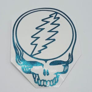 May include: A teal glitter sticker of the Grateful Dead's iconic skull and lightning bolt logo.