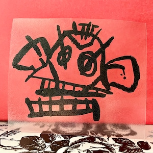 May include: Black and white line drawing of a cartoon face with a large mouth and two eyes. The drawing is on a clear, translucent sheet.