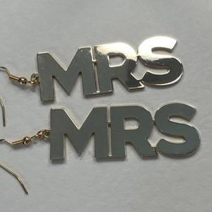 May include: Gold-tone earrings with the word "MRS" spelled out in large, bold letters. The earrings are dangle style with a hook closure.