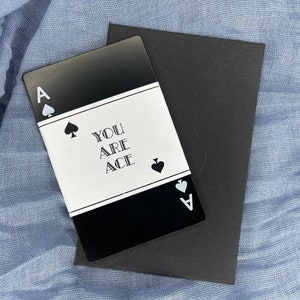Może przedstawiać: Czarna karta z białym obramowaniem i tekstem "You are Ace" w środku. Karta ma symbol pika w lewym g&oacute;rnym rogu i literę "A" w prawym dolnym rogu.