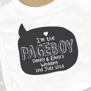 Puede incluir: Babero blanco con una burbuja de diálogo negra que dice "I'm the Pageboy Danny & Emily's Wedding 2nd July 2023".