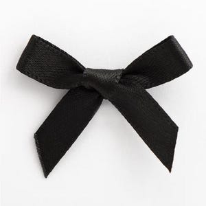 Może przedstawiać: Mała, czarna satynowa kokarda. Kokarda jest zawiązana na środku i ma dwie pętle i dwa ogony. Jest to klasyczny design, prawdopodobnie używany do pakowania prezentów, rękodzieła lub dekoracji.