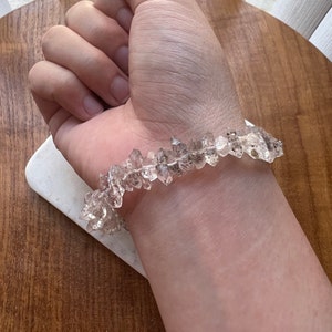 May include: A clear crystal bracelet made of faceted, pointed stones. The bracelet is worn on a person's wrist.