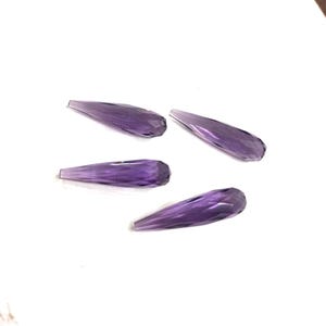 Könnte beinhalten: Vier facettierte, tropfenförmige Amethyst-Edelsteine. Die Edelsteine haben eine tiefviolette Farbe und ein poliertes, kristallines Aussehen. Sie sind auf einer weißen Oberfläche angeordnet.
