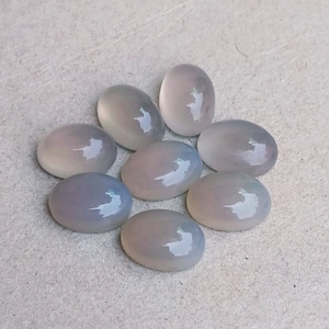 May include: Eight oval-shaped, translucent, light gray gemstones. The stones have a smooth, polished surface and are arranged in a loose circle.