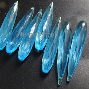 以下が含まれることがあります： 8つのファセットカットされたライトブルーの涙型のクリスタルビーズのグループ。ビーズの長さは約5cmです。