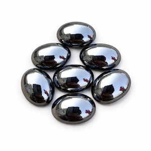May include: Seven polished, oval-shaped, dark gray stones arranged in a circular pattern. Each stone has a reflective, mirror-like surface, reflecting the surrounding environment. The stones are smooth and appear to be made of a dense material.