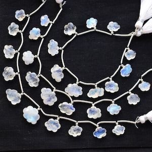 May include: Several strands of cloud-shaped moonstone beads, strung on silver wire. The beads are translucent, displaying blue and white colours. White tassels are at the ends. The background is black.