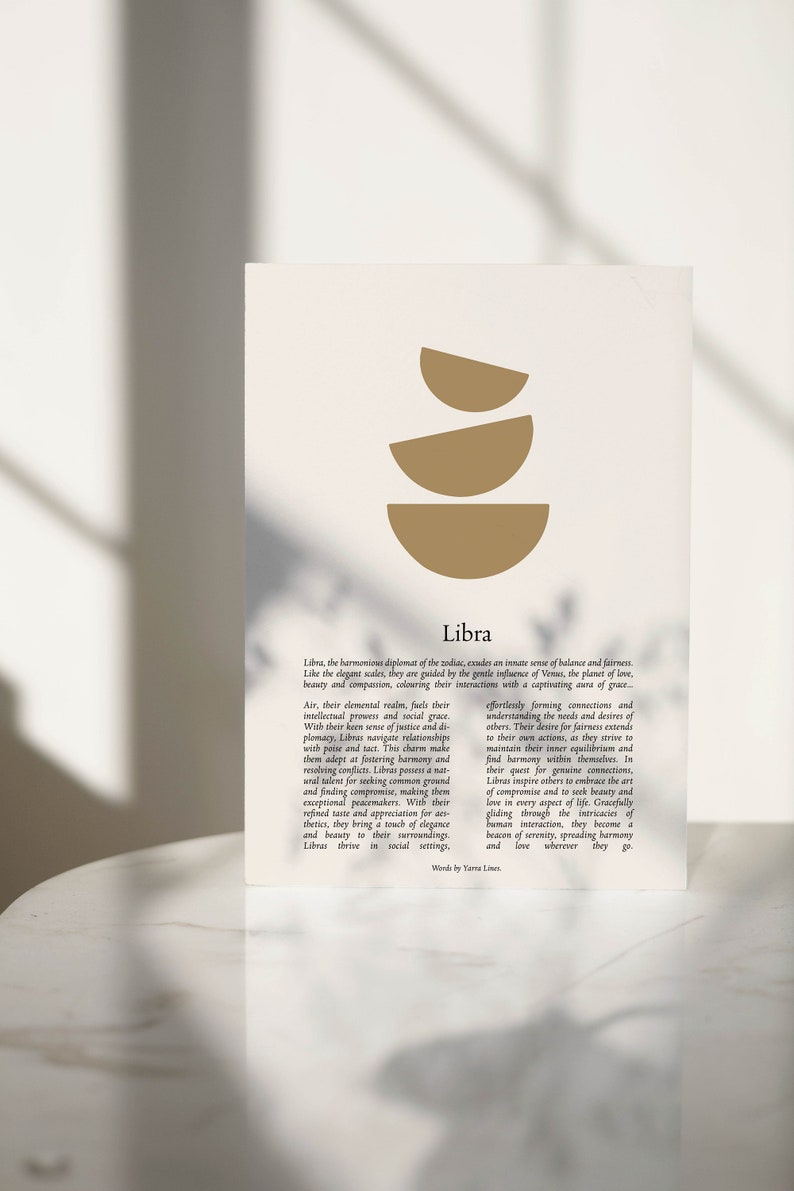 May include: A beige print with a gold abstract design of three stacked semi-circles, and the word "Libra" below. The text describes Libra's traits, including balance and fairness. The print is displayed on a white surface.