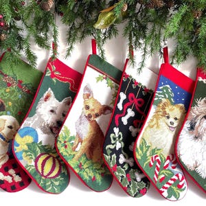 May include: Six needlepoint Christmas stockings featuring various dog breeds including a Labrador, Westie, Chihuahua, Pomeranian, and Shih Tzu, alongside festive patterns of candy canes, holly, and bones, all finished with red fabric trim.