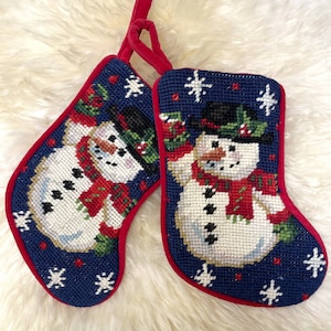 May include: Two blue and red Christmas stockings with a snowman design. The stockings are decorated with white snowflakes and red berries.
