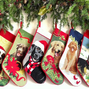 May include: Six needlepoint Christmas stockings featuring various dog breeds including a black Labrador, a golden retriever, and a Bernese mountain dog, each decorated with festive holiday elements like Santa hats, poinsettias, and winter scenery.
