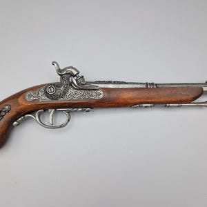 Könnte beinhalten: Eine antike Pistole im Silber- und Holzdesign mit aufwendigen Gravuren. Die Pistole hat einen Holzgriff und einen silbernen Lauf mit einem dekorativen Design.