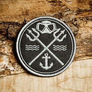 Könnte beinhalten: Ein gestickter Patch in Schwarz und Weiß mit einer Tauchermaske, gekreuzten Dreizacken, einem Anker und Wellen. Der Patch ist rund und hat einen weißen Rand.