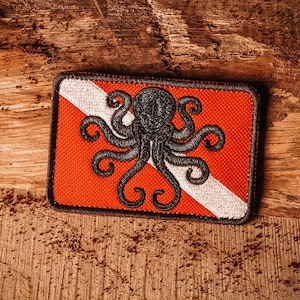 May include: A red and white scuba diving flag with a black octopus design. The flag is made of fabric and has a stitched border.