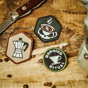 May include: Three embroidered patches with coffee themes. The first patch is green and features a coffee cup with steam rising from it. The second patch is beige and features a coffee pot. The third patch is green and black and features a coffee cup and the text "Morning Ritual".