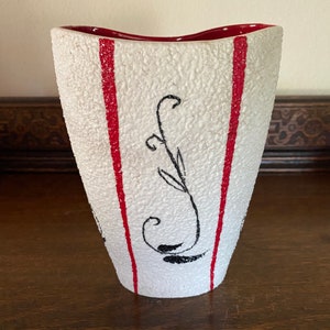 May include: White ceramic vase with a textured surface and red stripes. The vase has a black floral design.