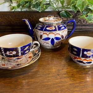May include: A vintage tea set comprising a teapot, teacup, saucer, and a small bowl. The set has a blue, white, and orange floral pattern with gold edging. The teapot has a lid and a curved spout. The teacup and bowl are round.