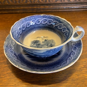 May include: A blue and white porcelain teacup and saucer set with a blue and white floral design. The saucer has a scalloped edge.