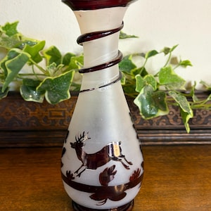 May include: A frosted glass vase with a burgundy rim and a decorative burgundy spiral design. The vase features a leaping deer and leaf design in burgundy. The vase is approximately 20 cm tall.